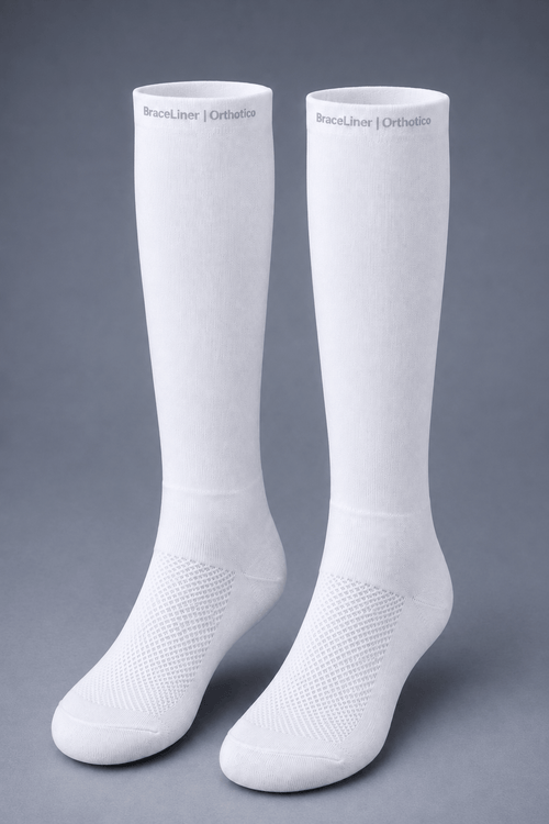 A pair of white knee-high orthopedic socks with textured knit arch support and ventilation zones, displayed on a neutral gray background. The brand name 'BraceLiner | Orthotics' is printed near the top cuff of each sock.